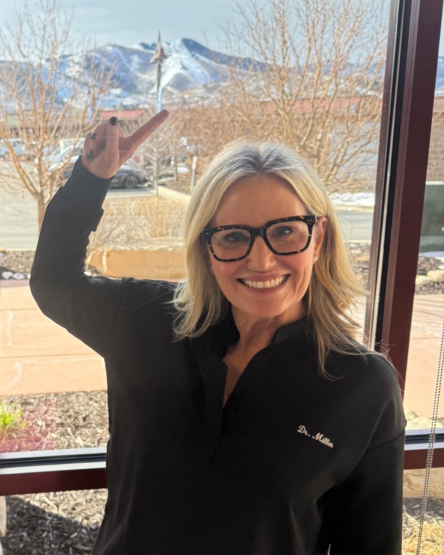 Dr. Juliana F. Miller smiling and pointing up at the snowy mountains outside the office window