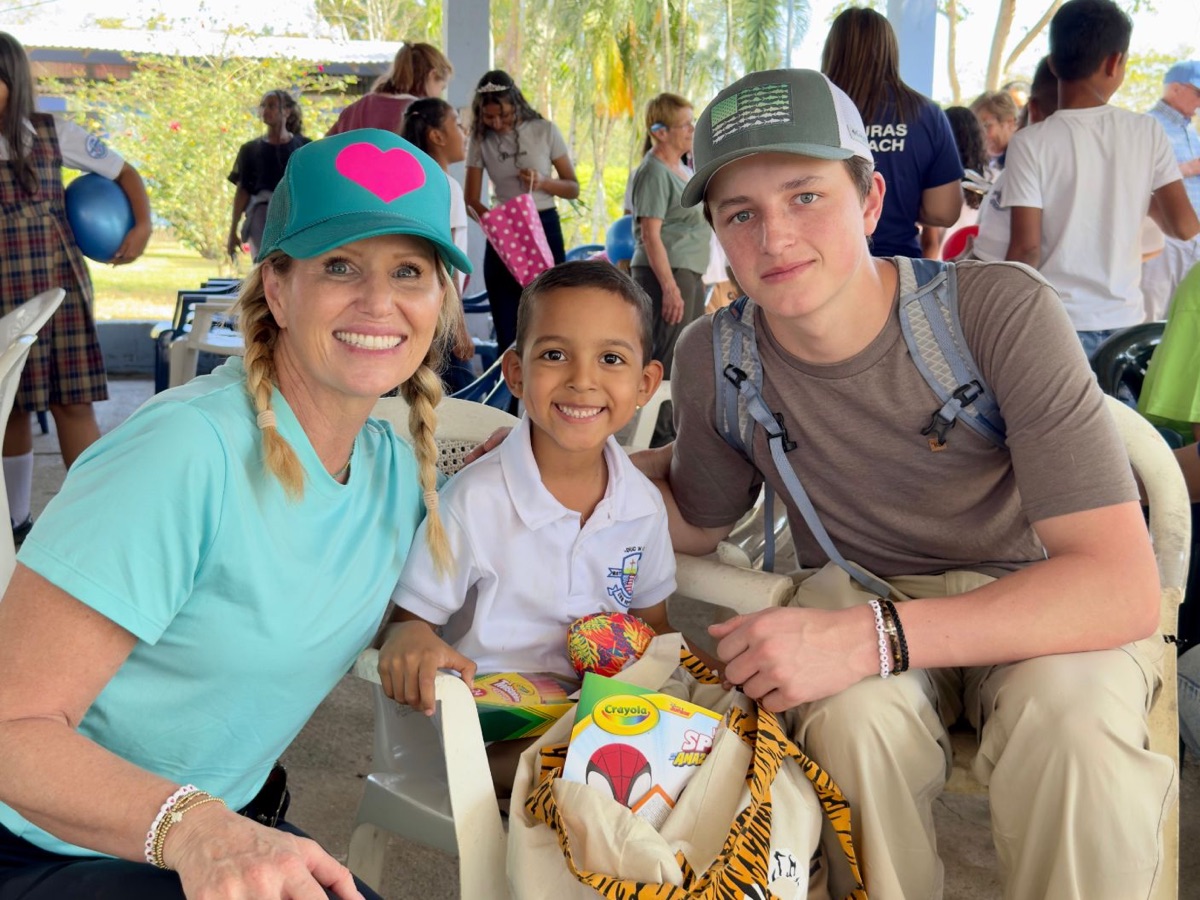 Dr. Juliana Miller smiling with a young schoolboy and a teen volunteer at an outdoor service event